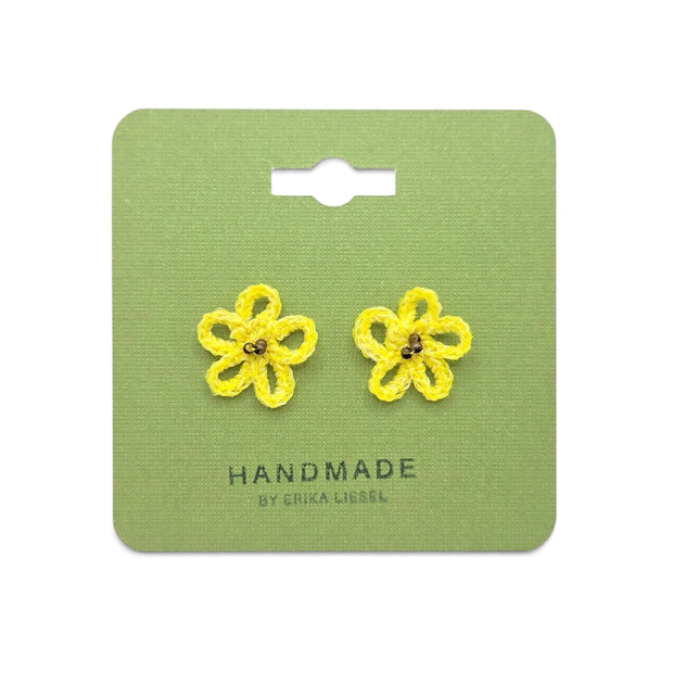 Handmade by Erika Liesel yellow daisy crochet stud earrings with glass bead centers on a green display card.