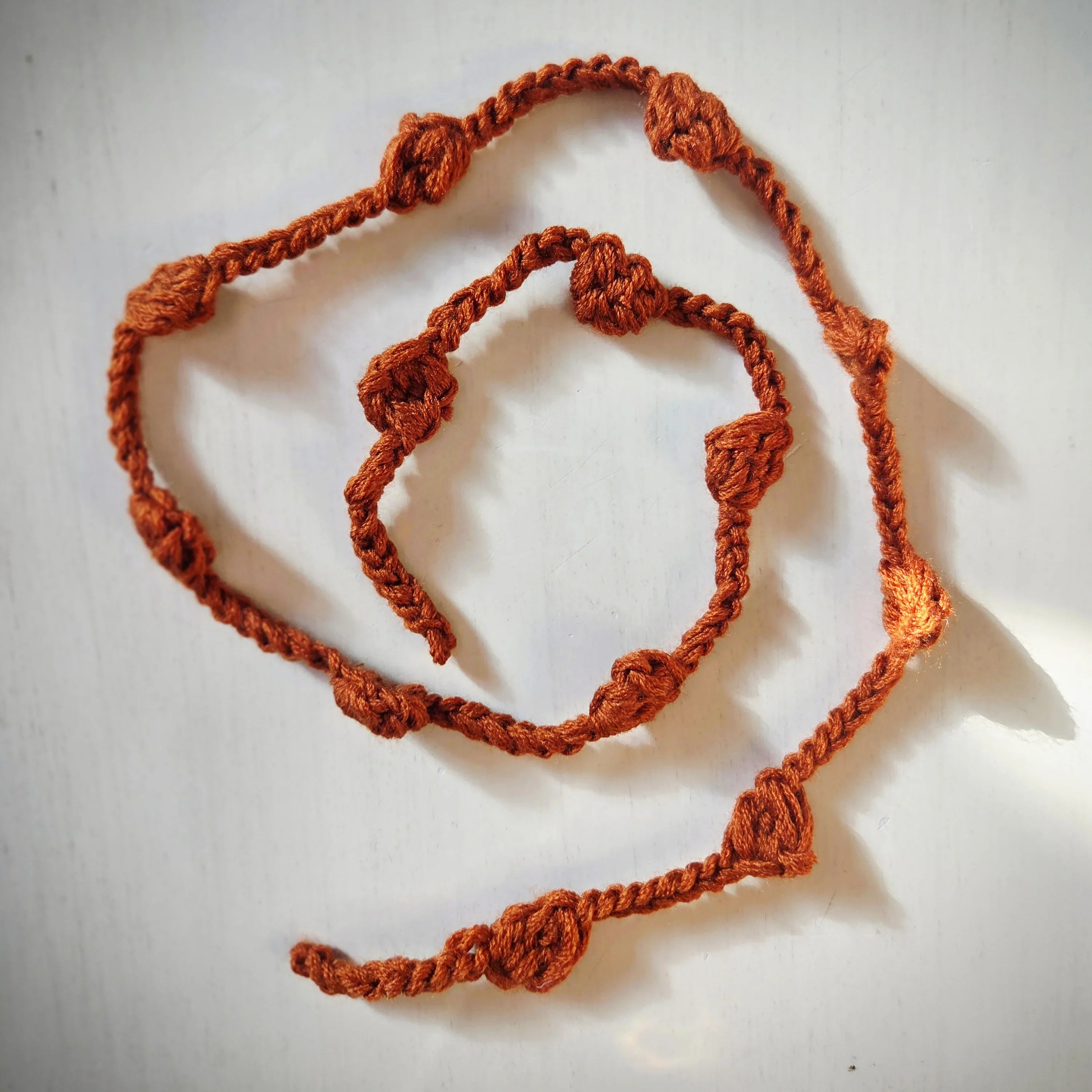 Handmade brown crochet bracelet and necklace with heart accents on white background