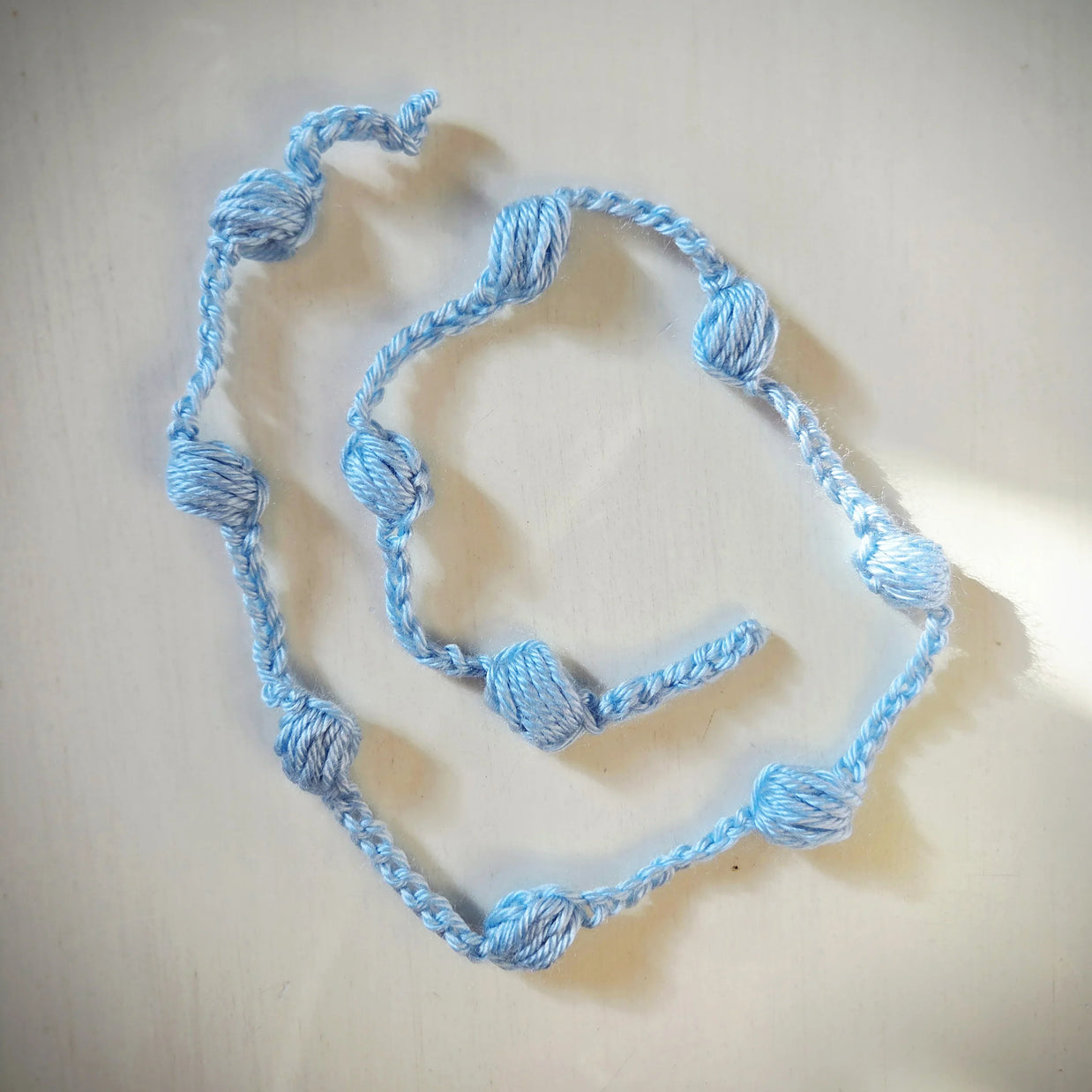Handmade light blue crochet necklace with yarn beads on a white surface