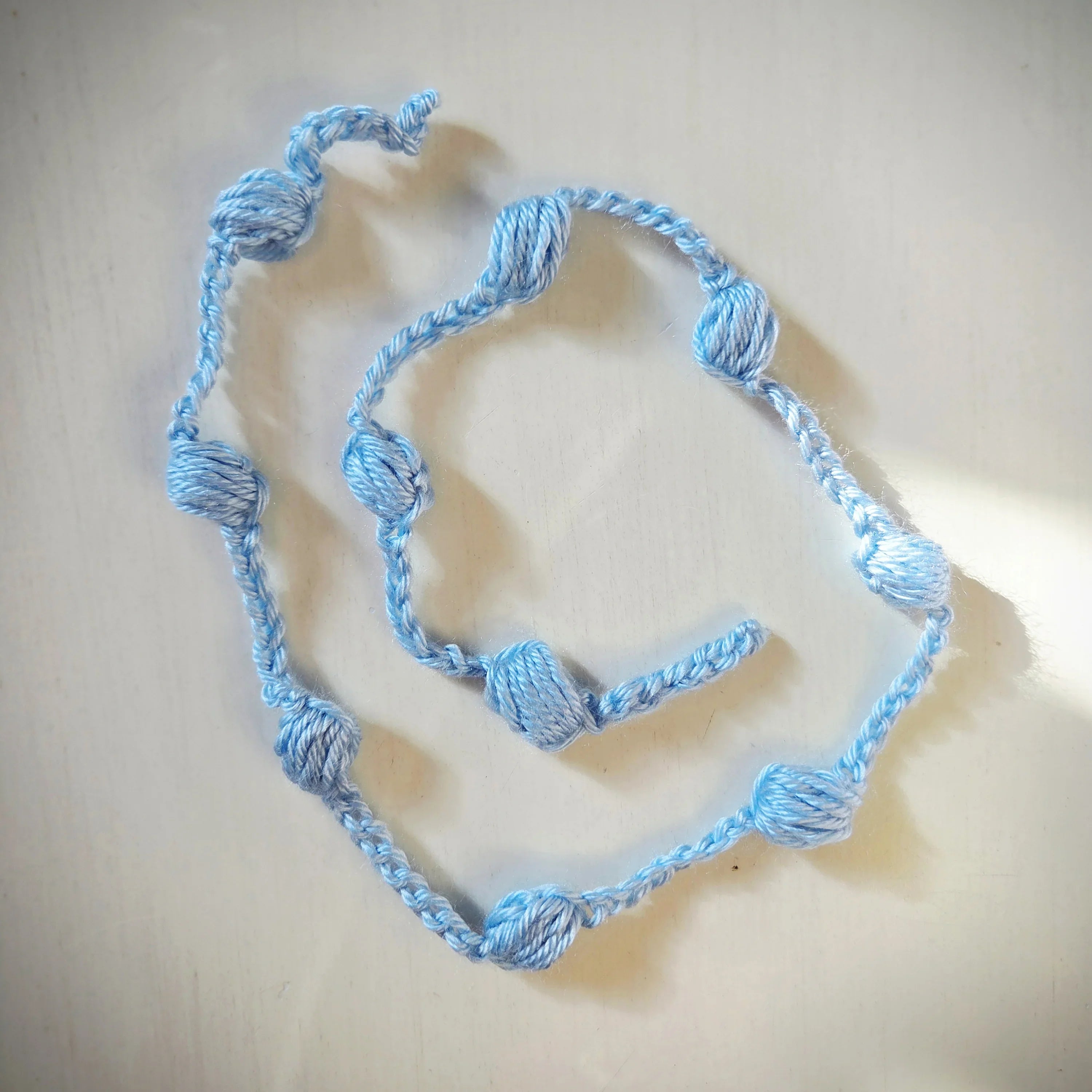 Handmade light blue crochet necklace with yarn beads on a white surface
