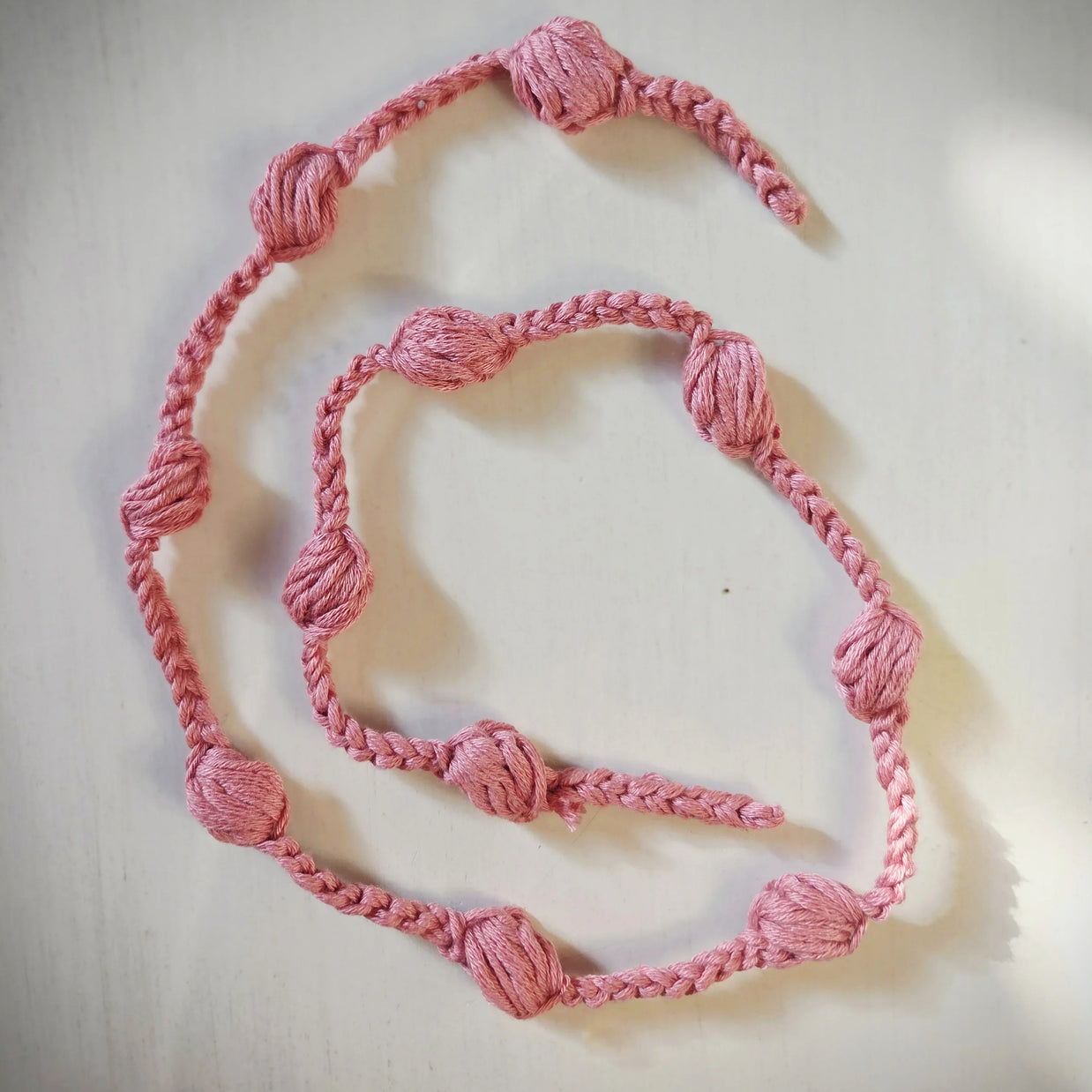 Handmade pink crochet garland with textured knots on a white surface