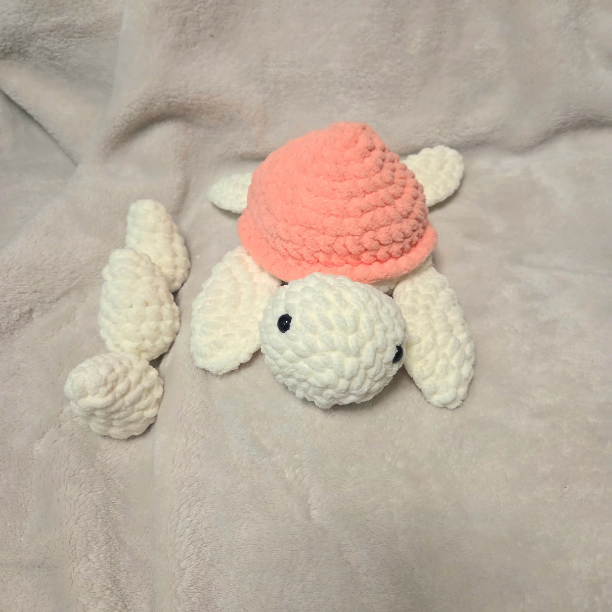 Handmade crochet turtle with pink shell and white limbs on soft blanket