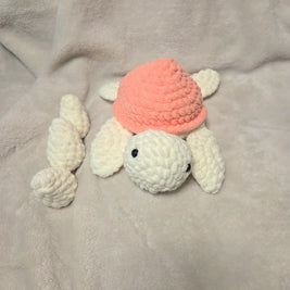 Handmade crochet turtle with pink shell and white limbs on soft blanket