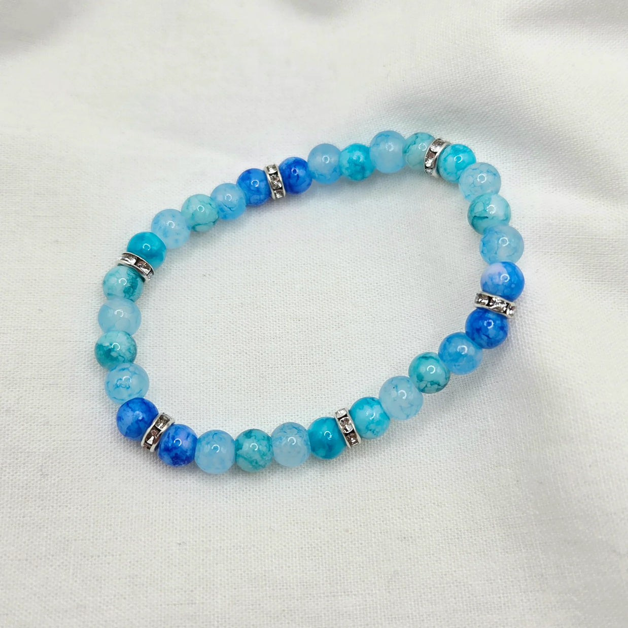 Blue beaded bracelet with silver accents on white fabric background