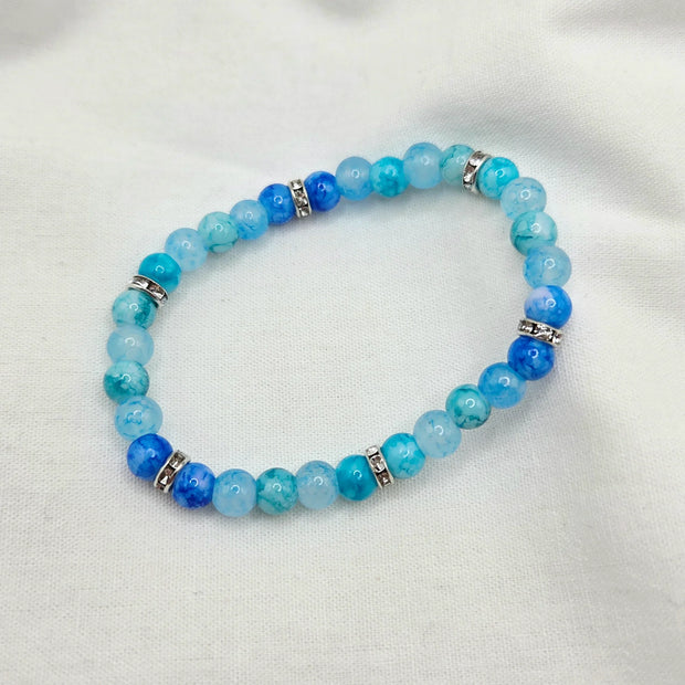 Blue beaded bracelet with silver accents on white fabric background