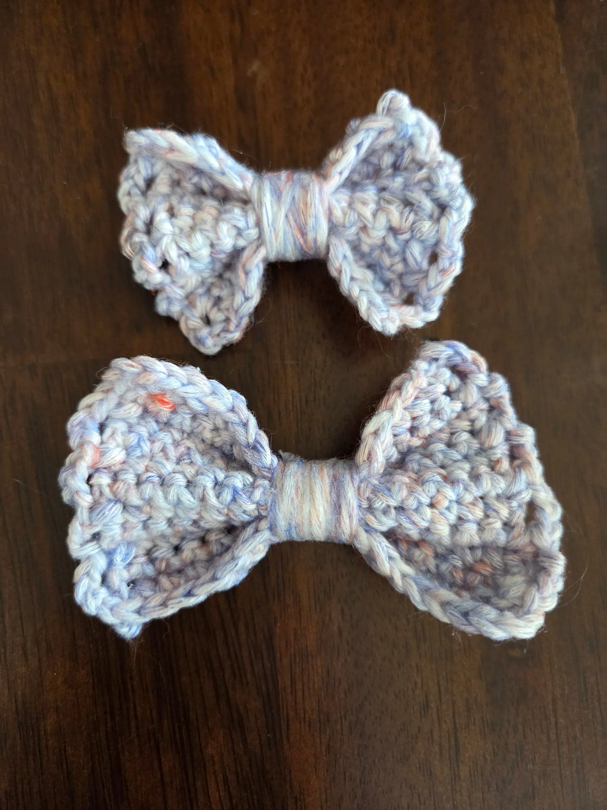 Two handmade crocheted yarn bows in light blue on a dark wooden surface