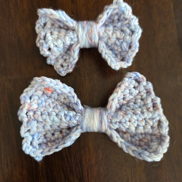 Two handmade crocheted yarn bows in light blue on a dark wooden surface