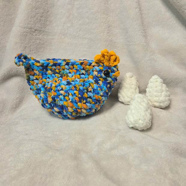 Handmade crochet bird with blue, yellow, and orange yarn, accompanied by white crocheted eggs on a soft blanket.
