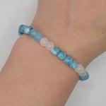 A beaded stretch bracelet worn on a wrist, featuring light blue marbled beads and translucent white beads, set against a plain light gray background.
