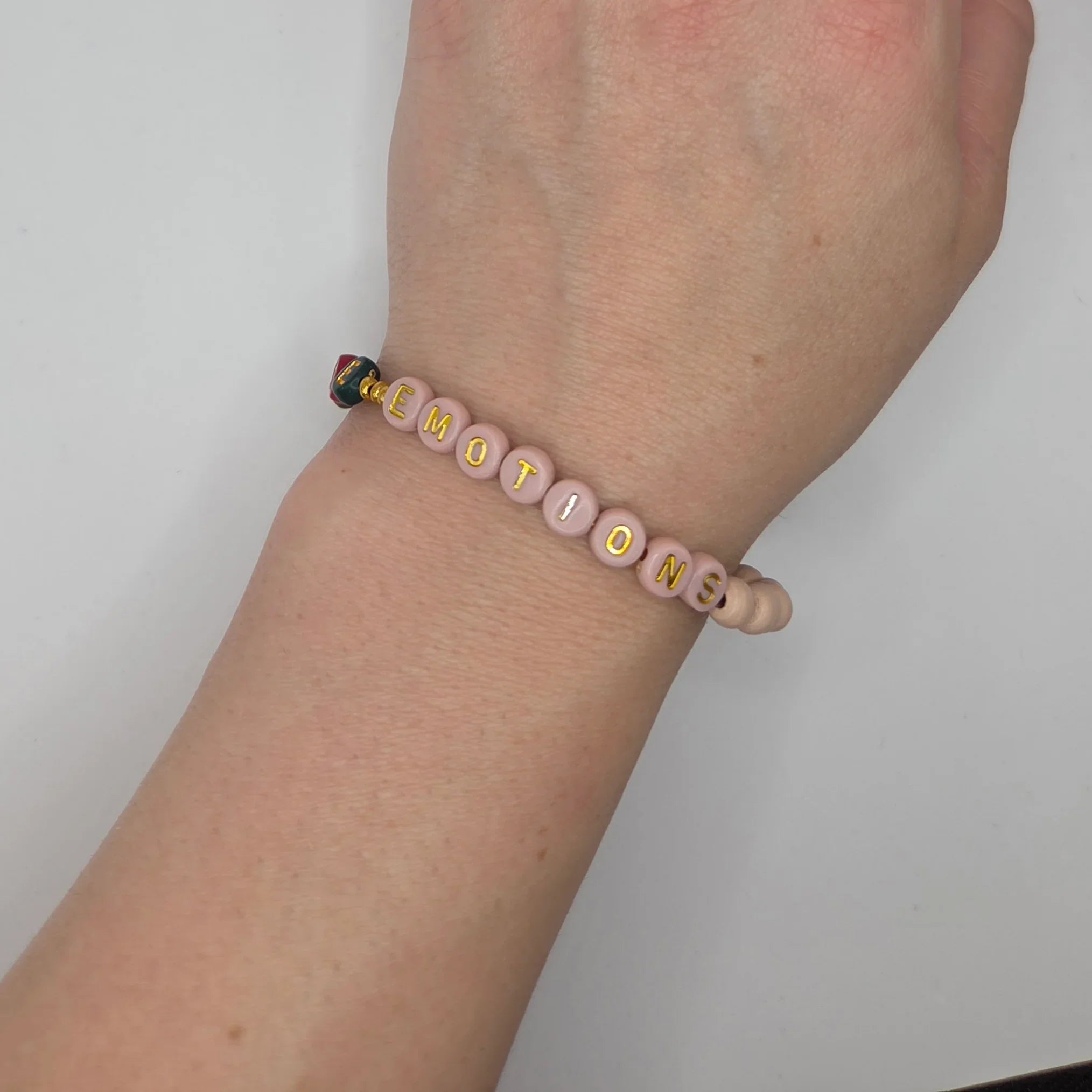 Pink beaded bracelet spelling 'EMOTIONS' with gold letters, worn on wrist
