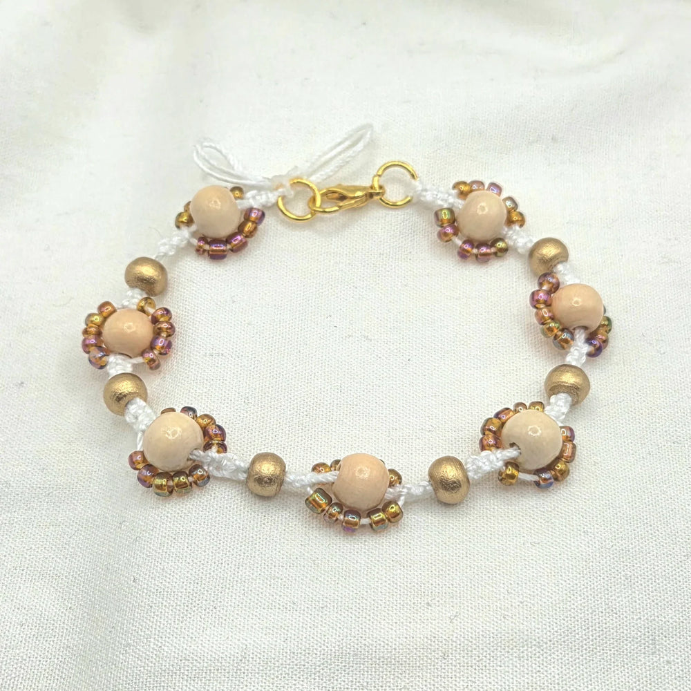 Handmade beaded bracelet with cream wood beads, gold accents, and iridescent seed beads on white cord