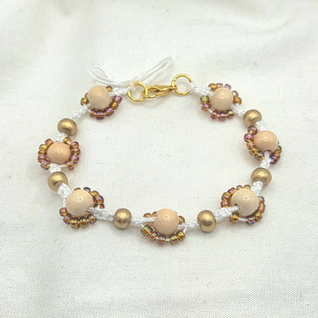 Handmade beaded bracelet with cream wood beads, gold accents, and iridescent seed beads on white cord