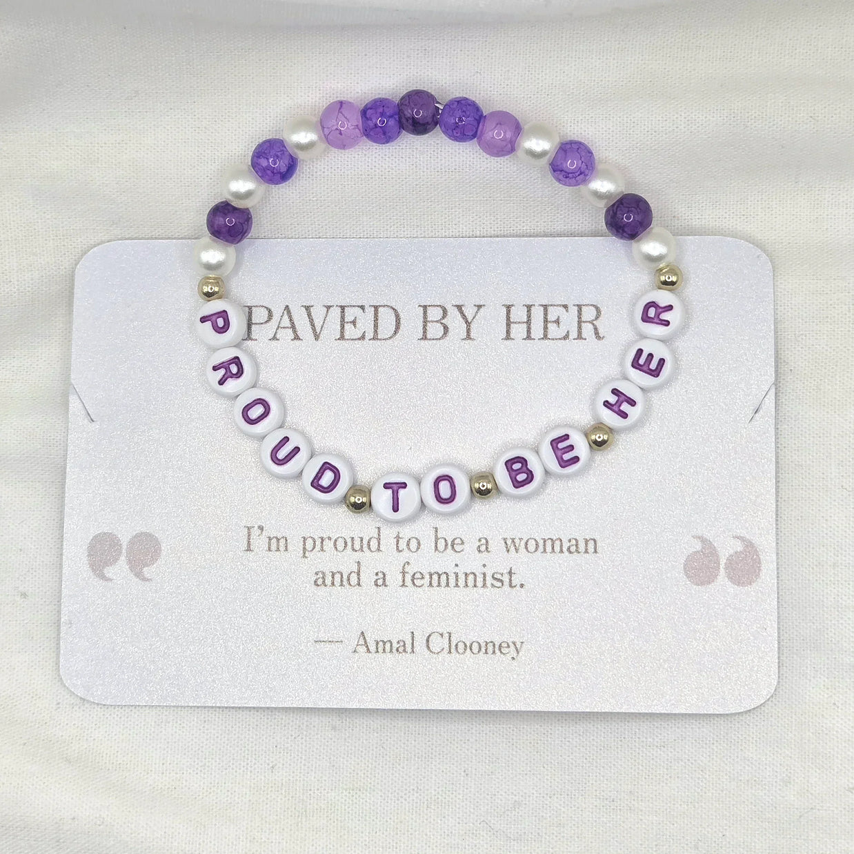 Purple and white beaded bracelet with 'PROUD TO BE HER' letter beads, displayed on quote card
