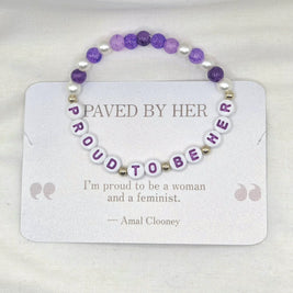 Purple and white beaded bracelet with 'PROUD TO BE HER' letter beads, displayed on quote card