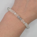 A beaded stretch bracelet worn on a wrist, featuring translucent white and frosted gray beads with clear faceted crystal accents, set against a plain light gray background.