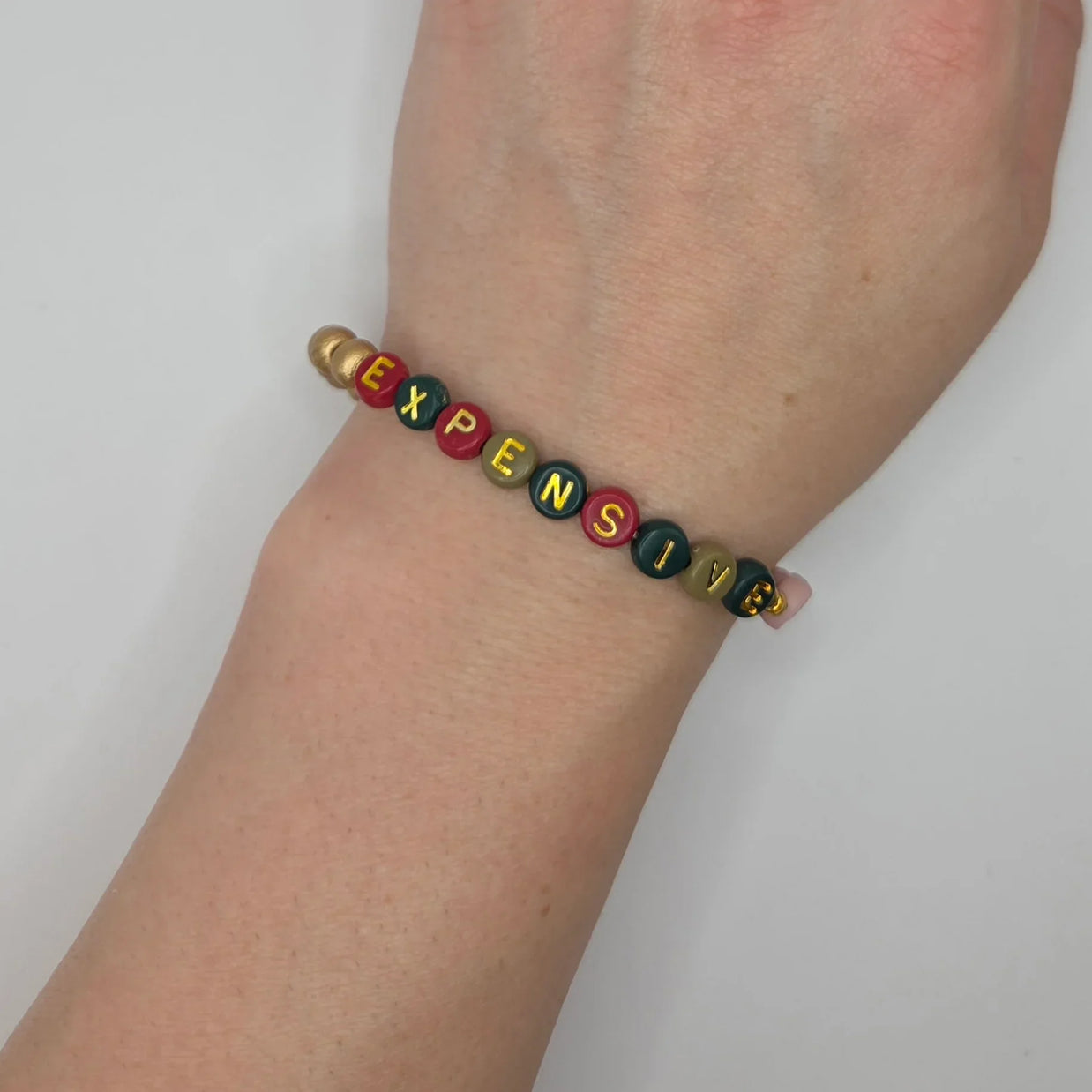 Colorful beaded bracelet spelling 'EXPENSIVE' on wrist, handmade gift for cozy style