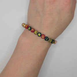 Colorful beaded bracelet spelling 'EXPENSIVE' on wrist, handmade gift for cozy style