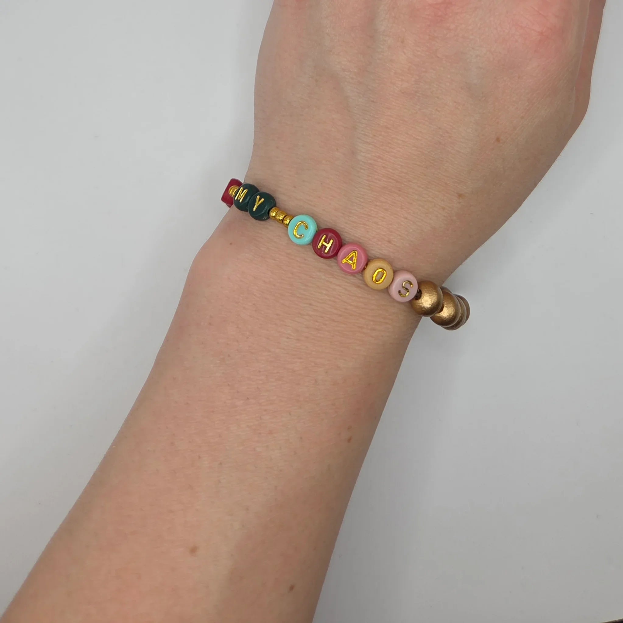 Colorful beaded bracelet spelling 'MY CHAOS' on wrist, handmade with gold letter beads and pastel accents