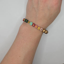 Colorful beaded bracelet spelling 'MY CHAOS' on wrist, handmade with gold letter beads and pastel accents