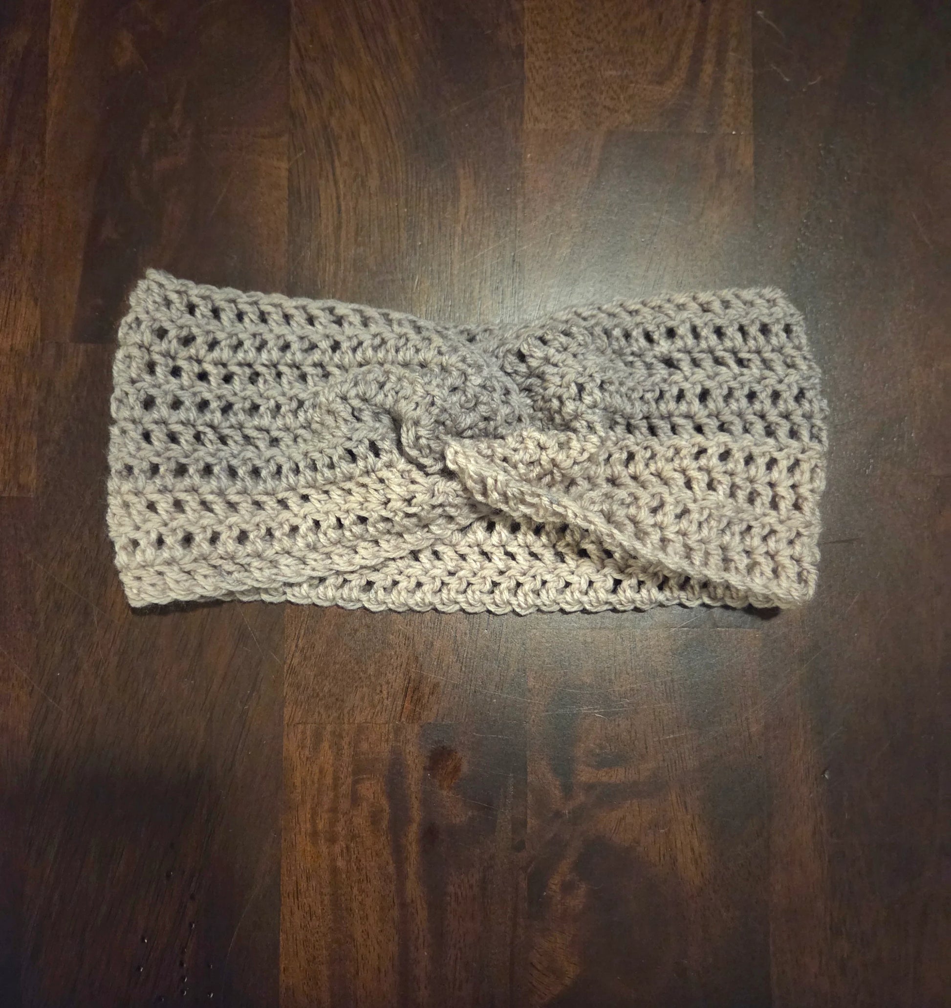 Beige crocheted headband with twist detail on dark wood surface