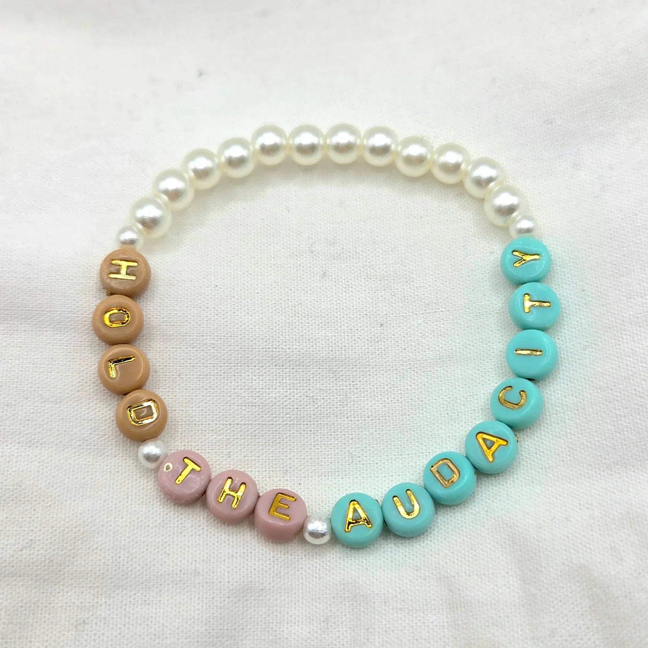 Handmade beaded bracelet with 'FOLLOW THE AUDACITY' in pastel & gold letters, pearl accents, cozy gift idea