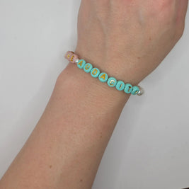Handmade beaded bracelet spelling 'HEAUDACITY' in gold letters on mint and pink beads, worn on wrist.
