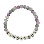 A beaded stretch bracelet on a light gray background, featuring marbled gray and pink beads, white beads spelling 'KIND SOUL' with a small black heart, and a clear elastic band.