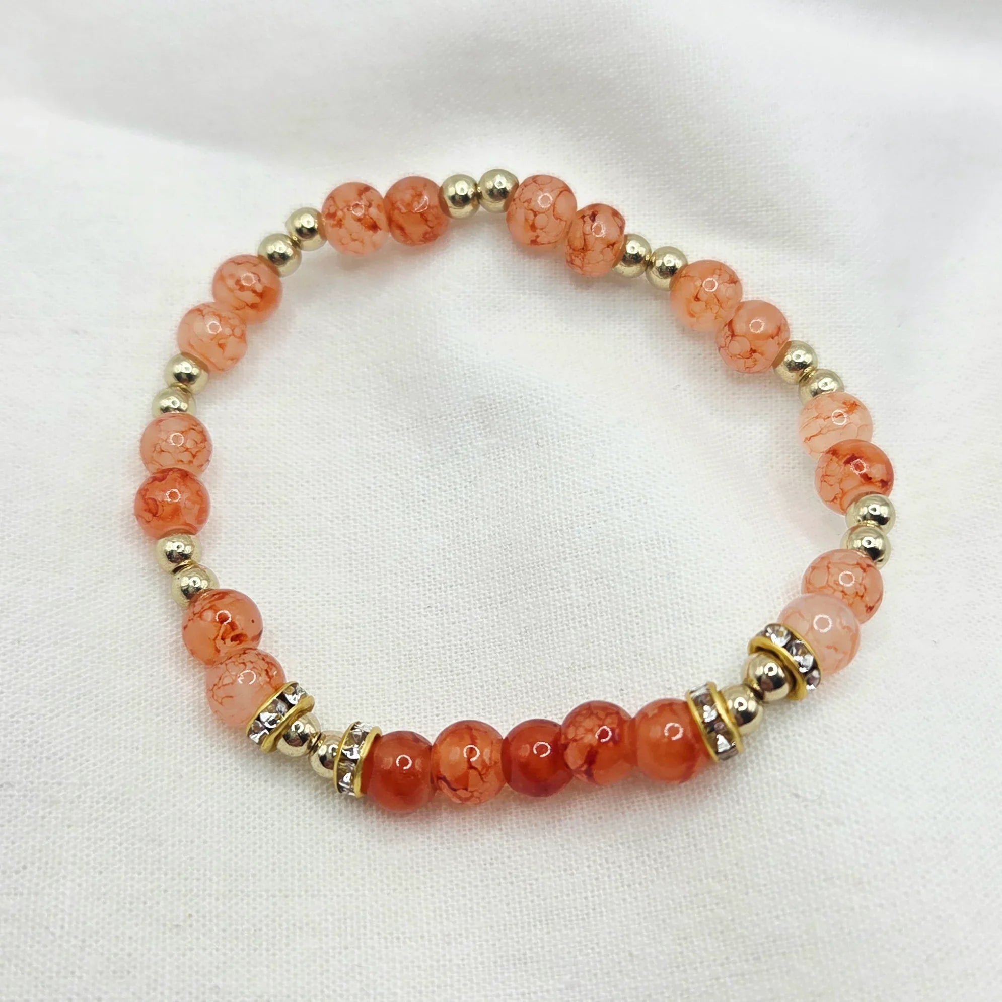 Coral and gold beaded bracelet with crystal accents on white fabric background