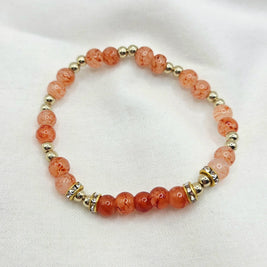 Coral and gold beaded bracelet with crystal accents on white fabric background