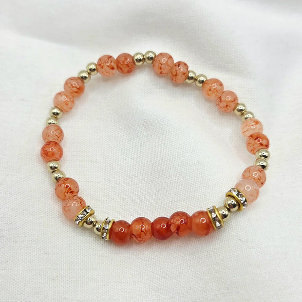 Coral and gold beaded bracelet with crystal accents on white fabric background
