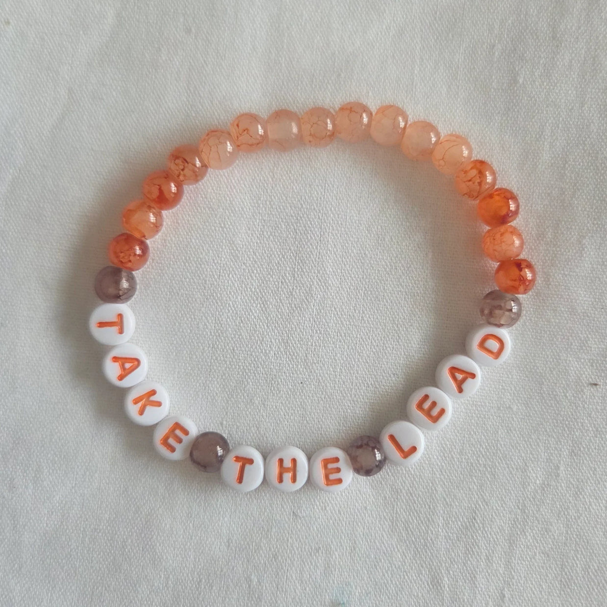 Take the Lead beaded bracelet with peach and white letter beads on fabric background