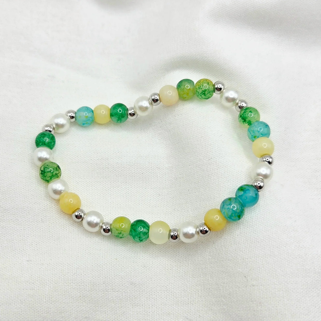 Handmade beaded bracelet with green, yellow, and white pearls on a soft fabric background