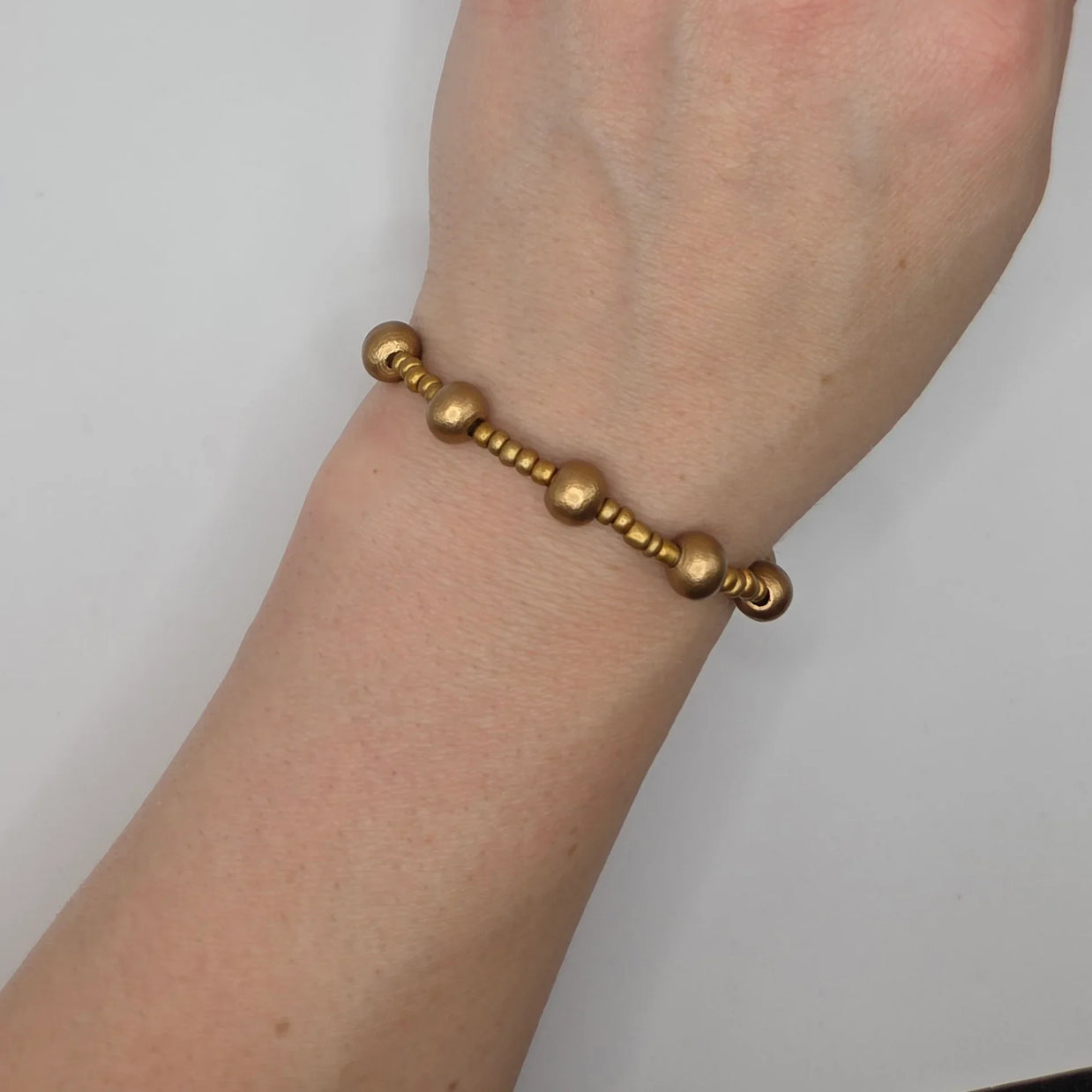 Gold beaded bracelet with textured spheres and small beads, worn on wrist for everyday style.