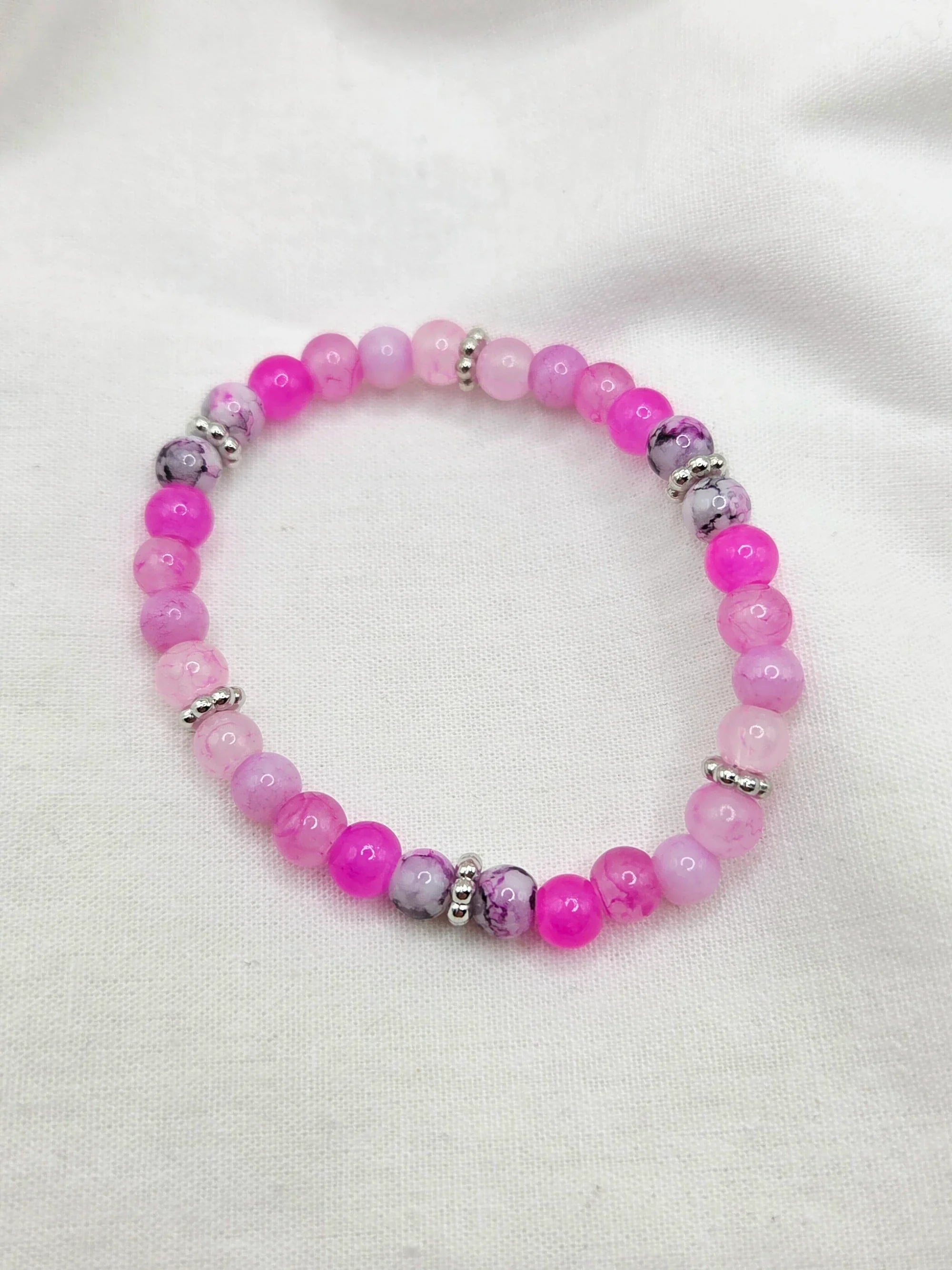 Pink and purple beaded bracelet with silver accents on white fabric background