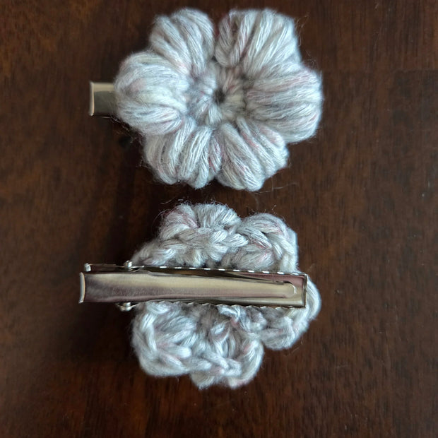 Handmade crochet flower hair clips with metal clasps on a dark wooden surface