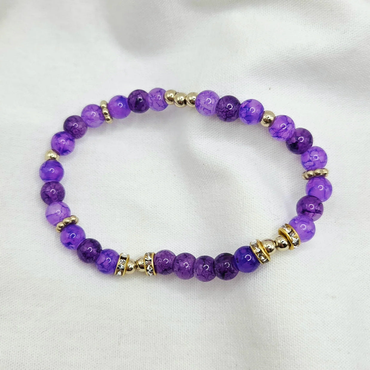 Purple beaded bracelet with gold accents and crystal details on white fabric