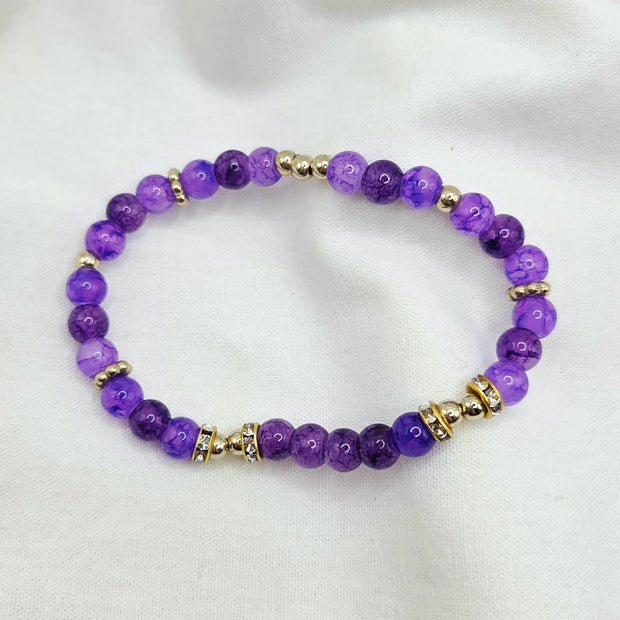 Purple beaded bracelet with gold accents and crystal details on white fabric