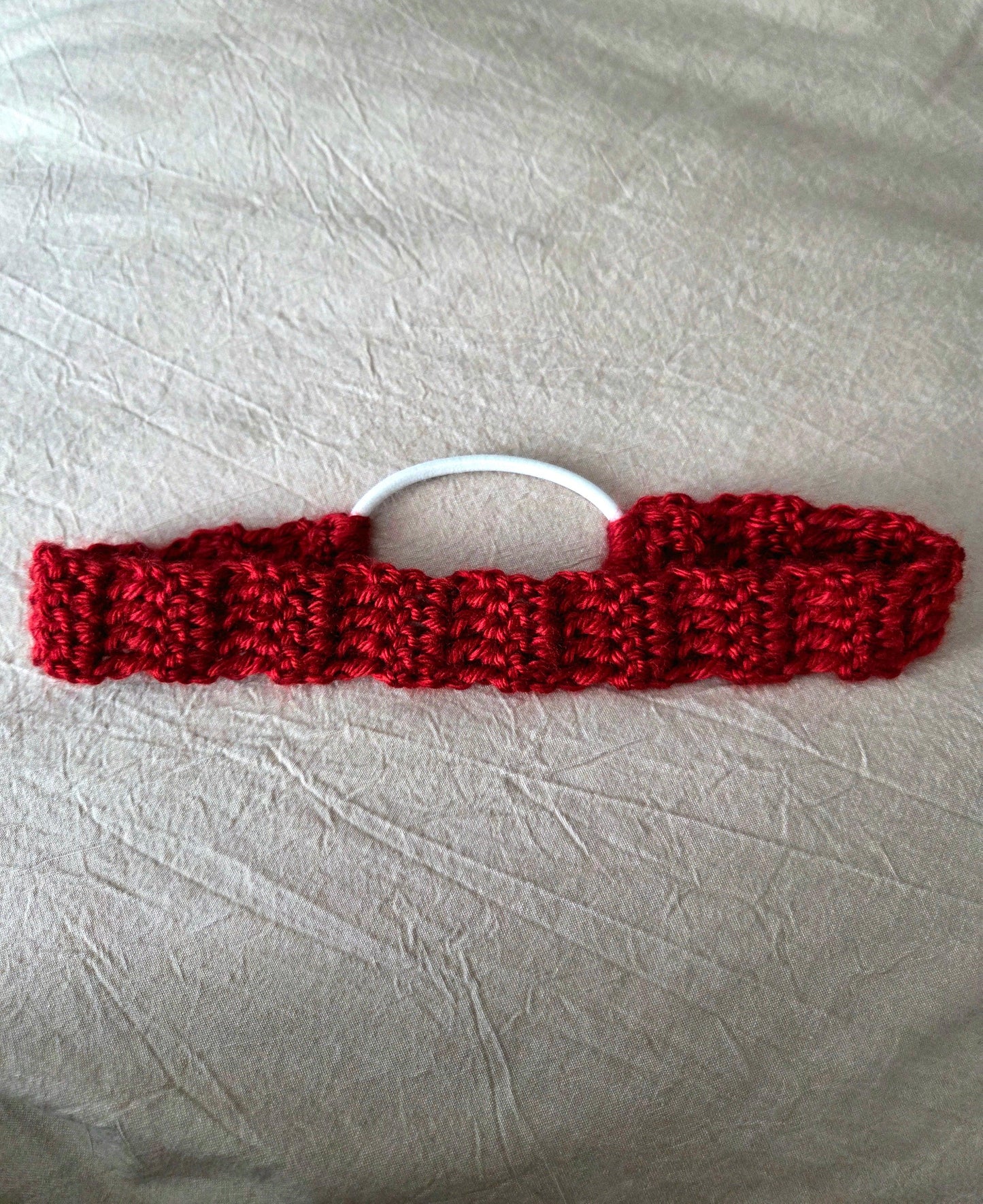 Handmade red crochet hair tie with white elastic on light fabric background