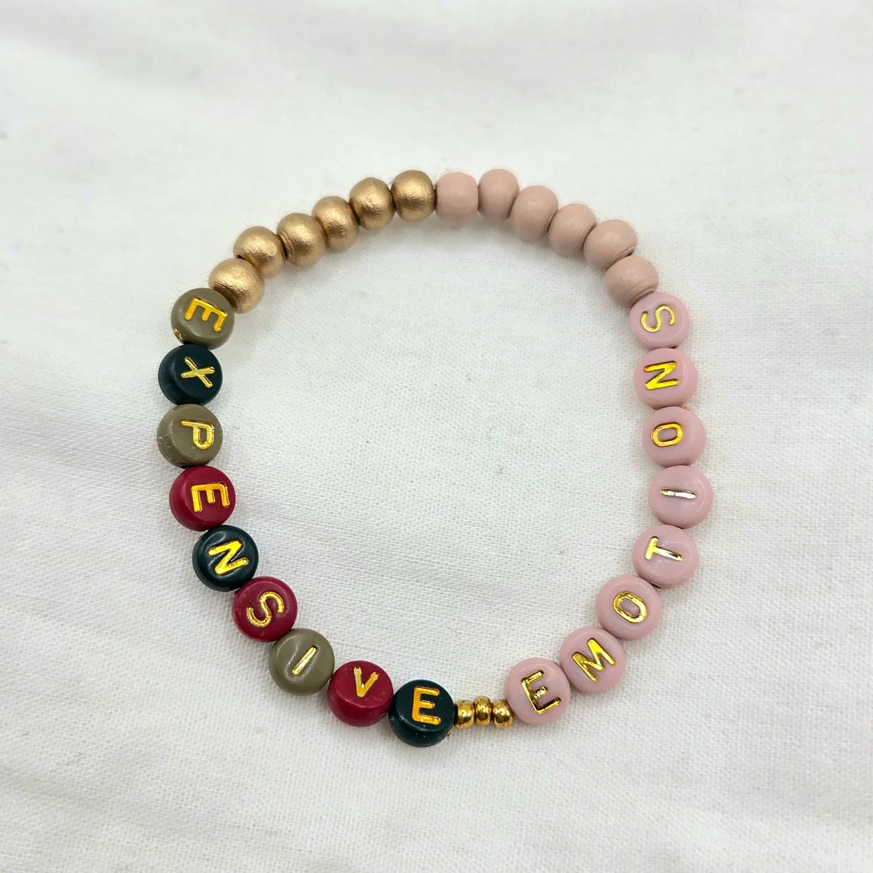 Handmade beaded bracelet with 'EXPENSIVE EMOTIONS' in colorful letters, gold accents, soft pink beads
