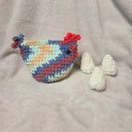 Handmade crochet chicken with colorful pattern and three white crocheted eggs on soft blanket