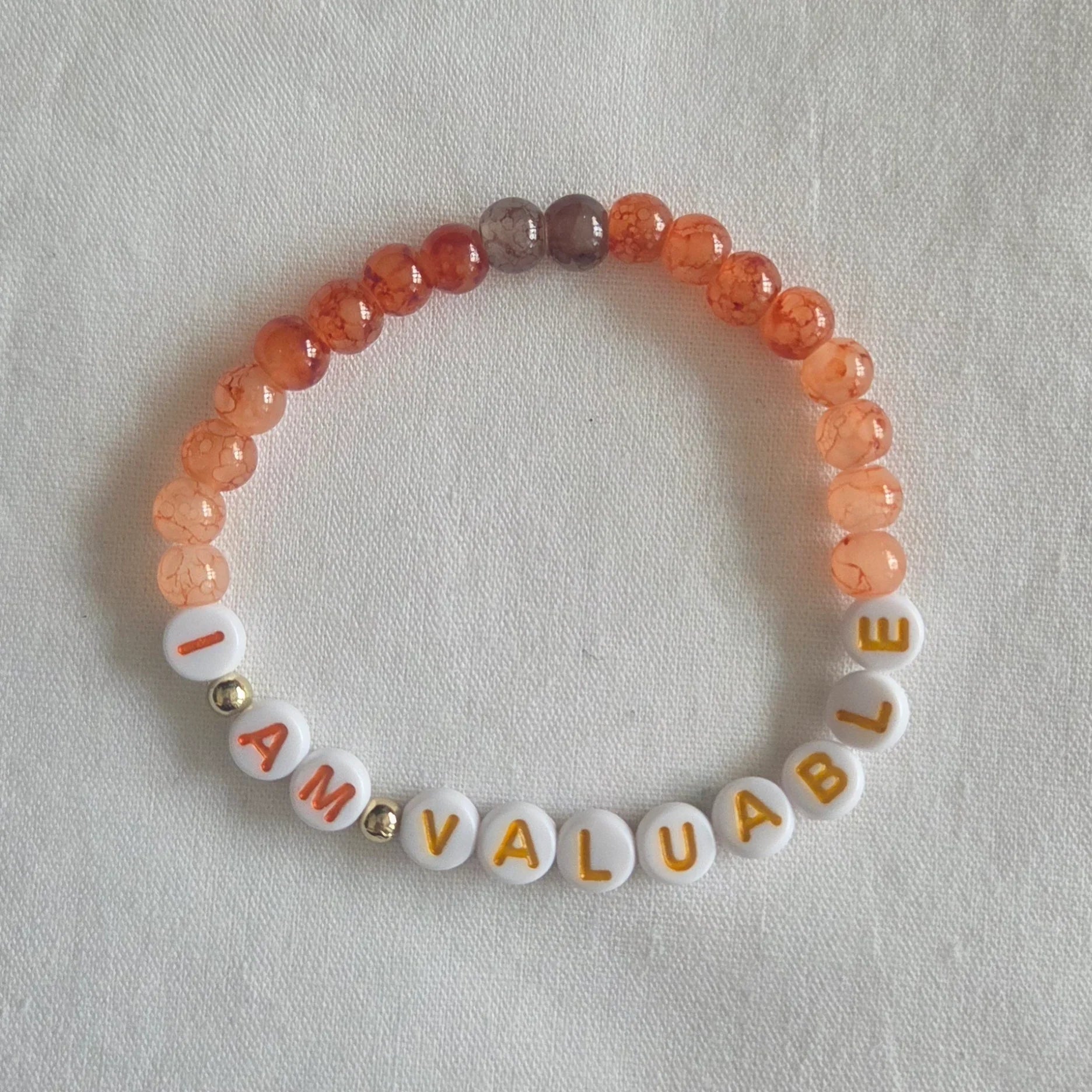 I AM VALUABLE beaded bracelet with orange and white beads on a soft fabric background