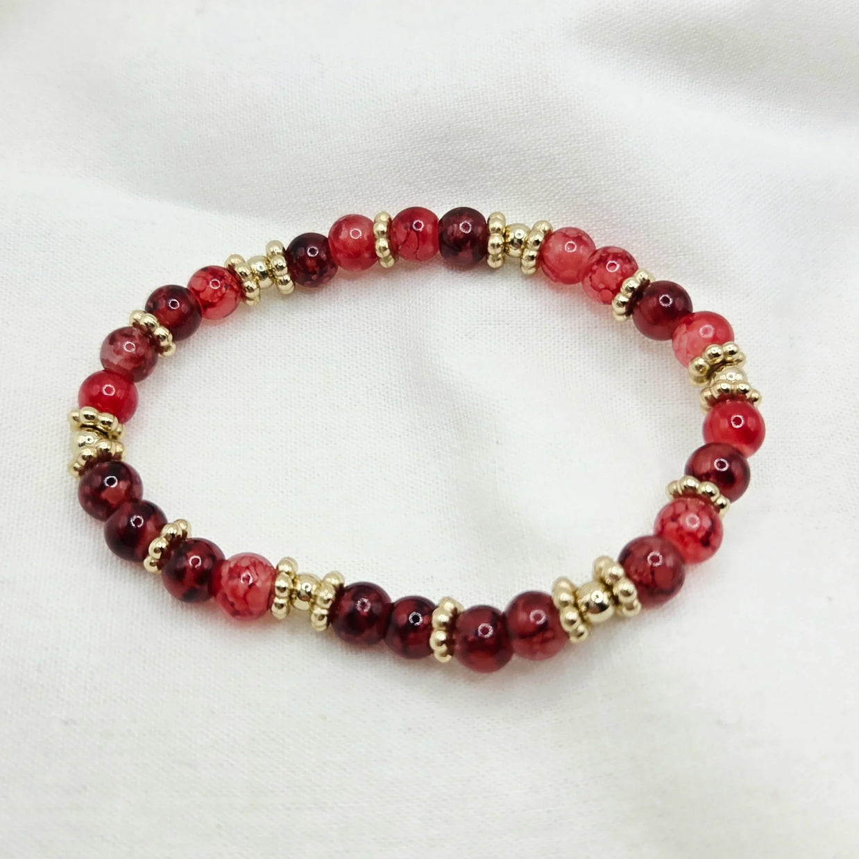 Red and gold beaded bracelet on white fabric background