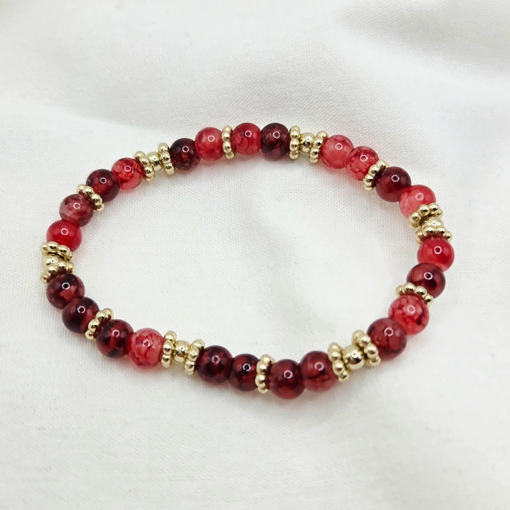 Red and gold beaded bracelet on white fabric background
