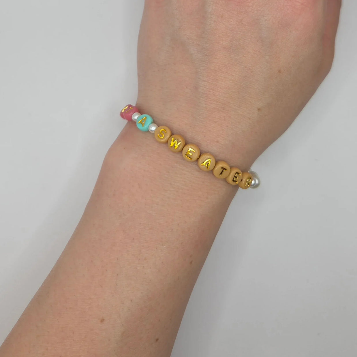 Handmade beaded bracelet spelling 'I A SWEATER' with colorful letter beads and pearls, cozy accessory.