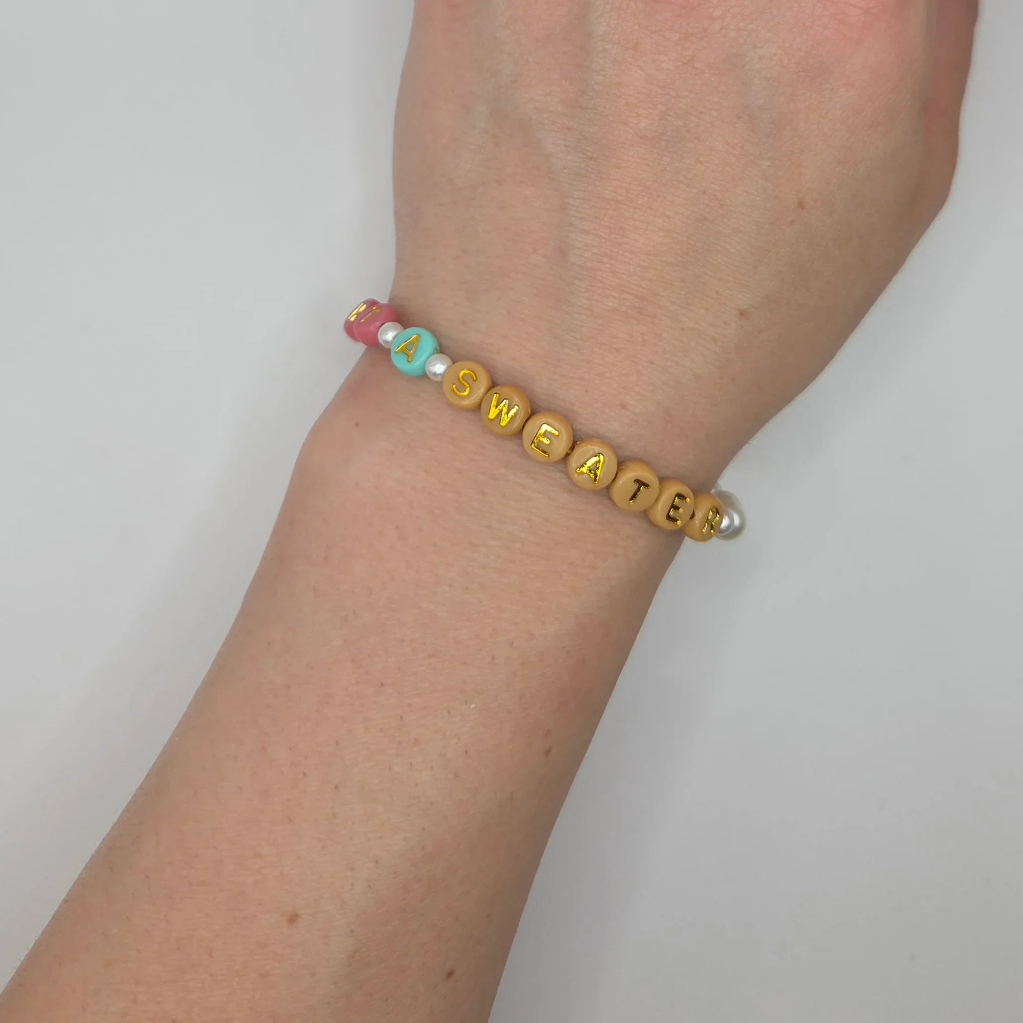 Handmade beaded bracelet spelling 'I A SWEATER' with colorful letter beads and pearls, cozy accessory.