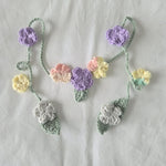 Handmade crochet flower garland with pastel blooms and green leaves, perfect for cozy home decor.