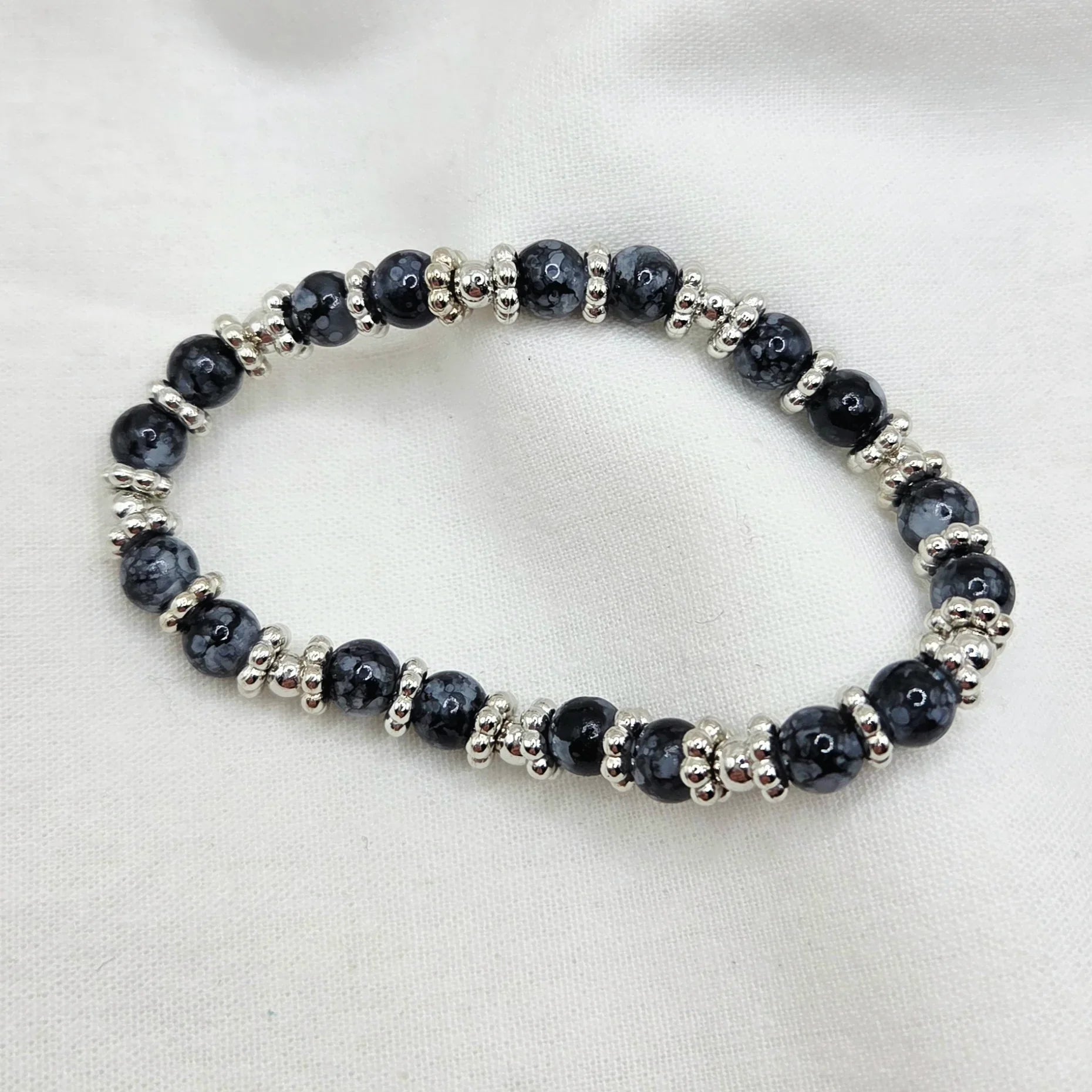 Black and silver beaded stretch bracelet on white fabric background