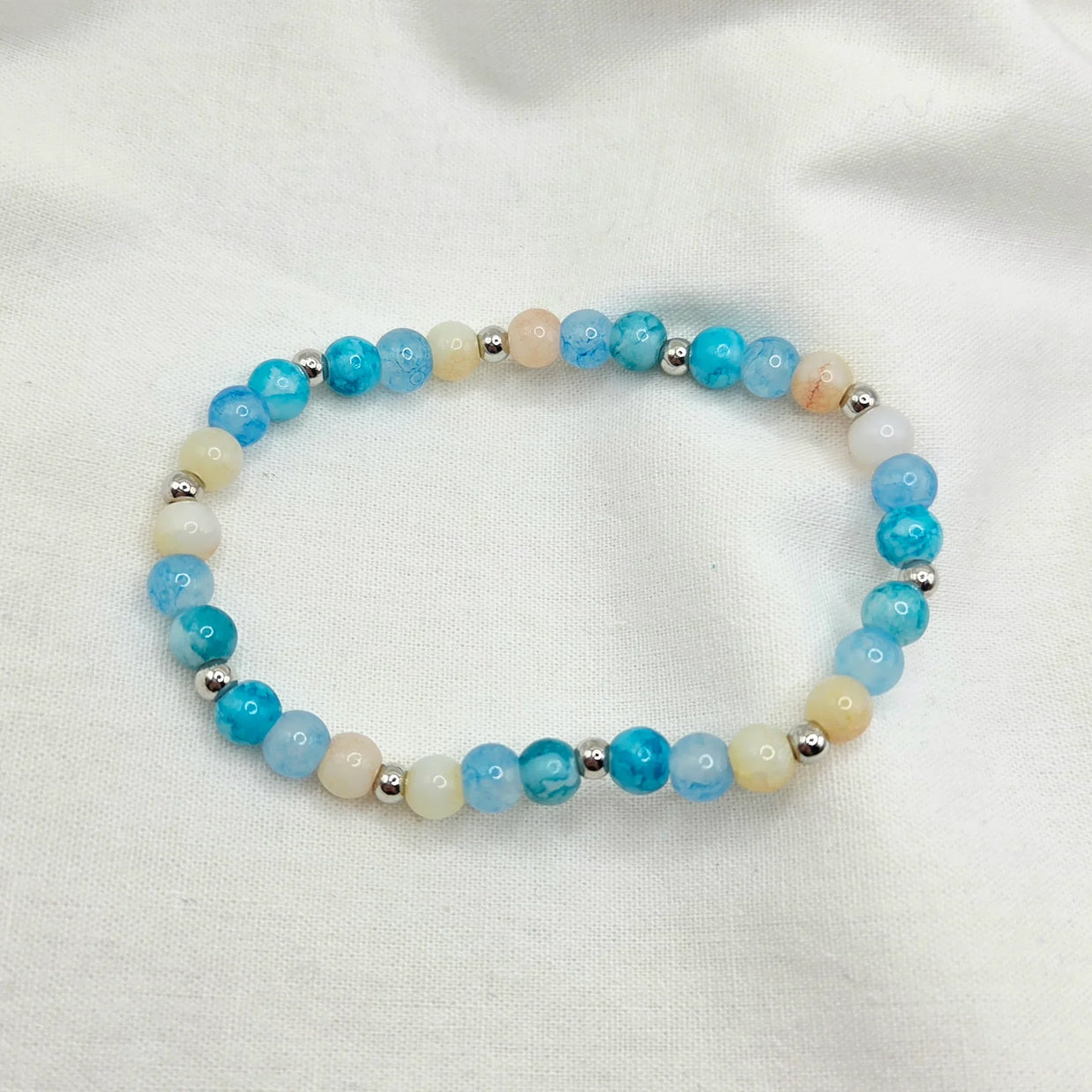 Blue and cream beaded bracelet with silver accents on white fabric