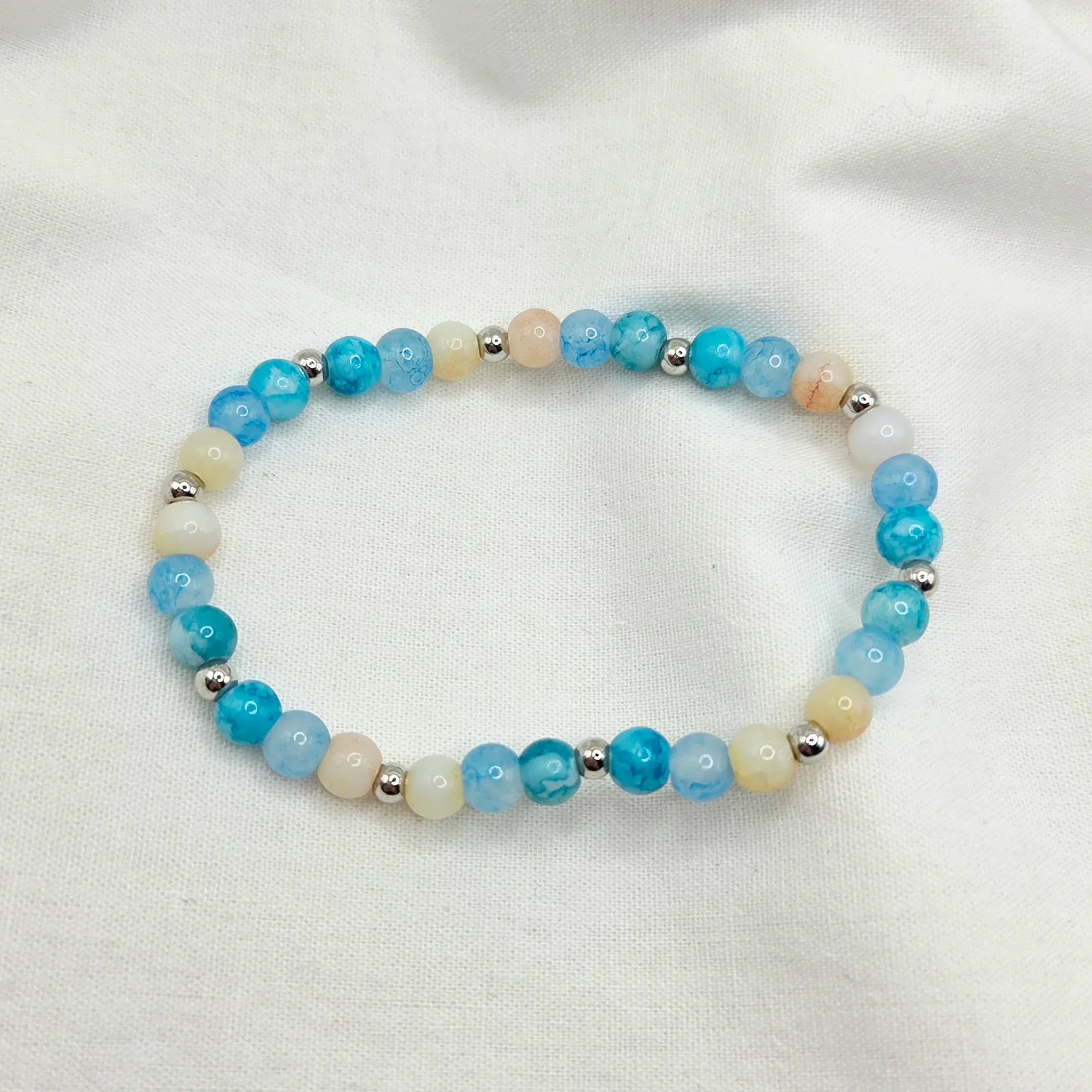 Blue and cream beaded bracelet with silver accents on white fabric