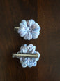 Two handmade light purple crochet flower hair clips on a dark wooden surface